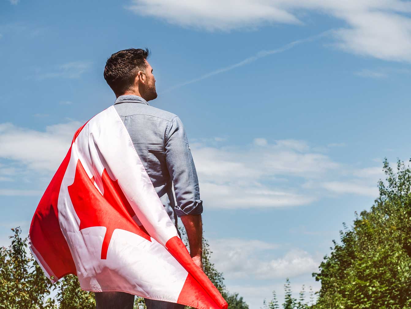 homme-seduisant-tenant-drapeau-canadien-fond-ciel-bleu-par-journee-claire-ensoleillee-vue-dos-gros-plan-concept-fete-nationale1